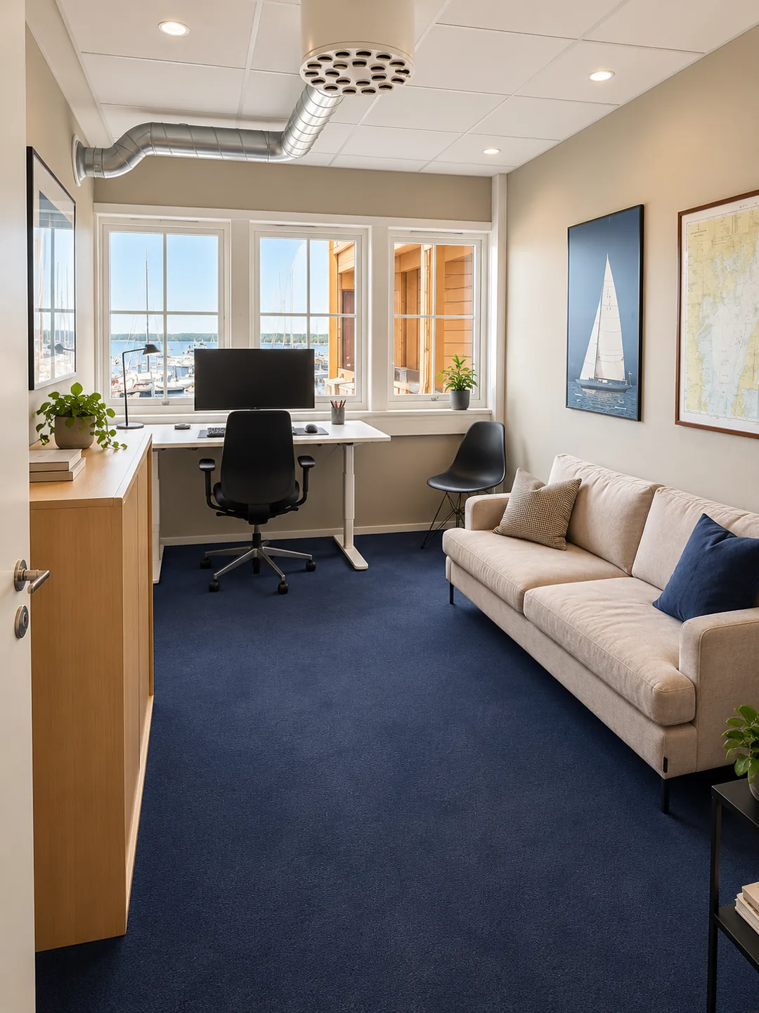 Møblert cellekontor med arbeidsbord, sofa og utsikt over båthavnen